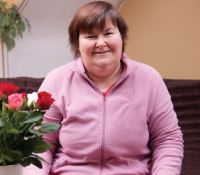 Woman with a pink blouse smiling beside flowers vase