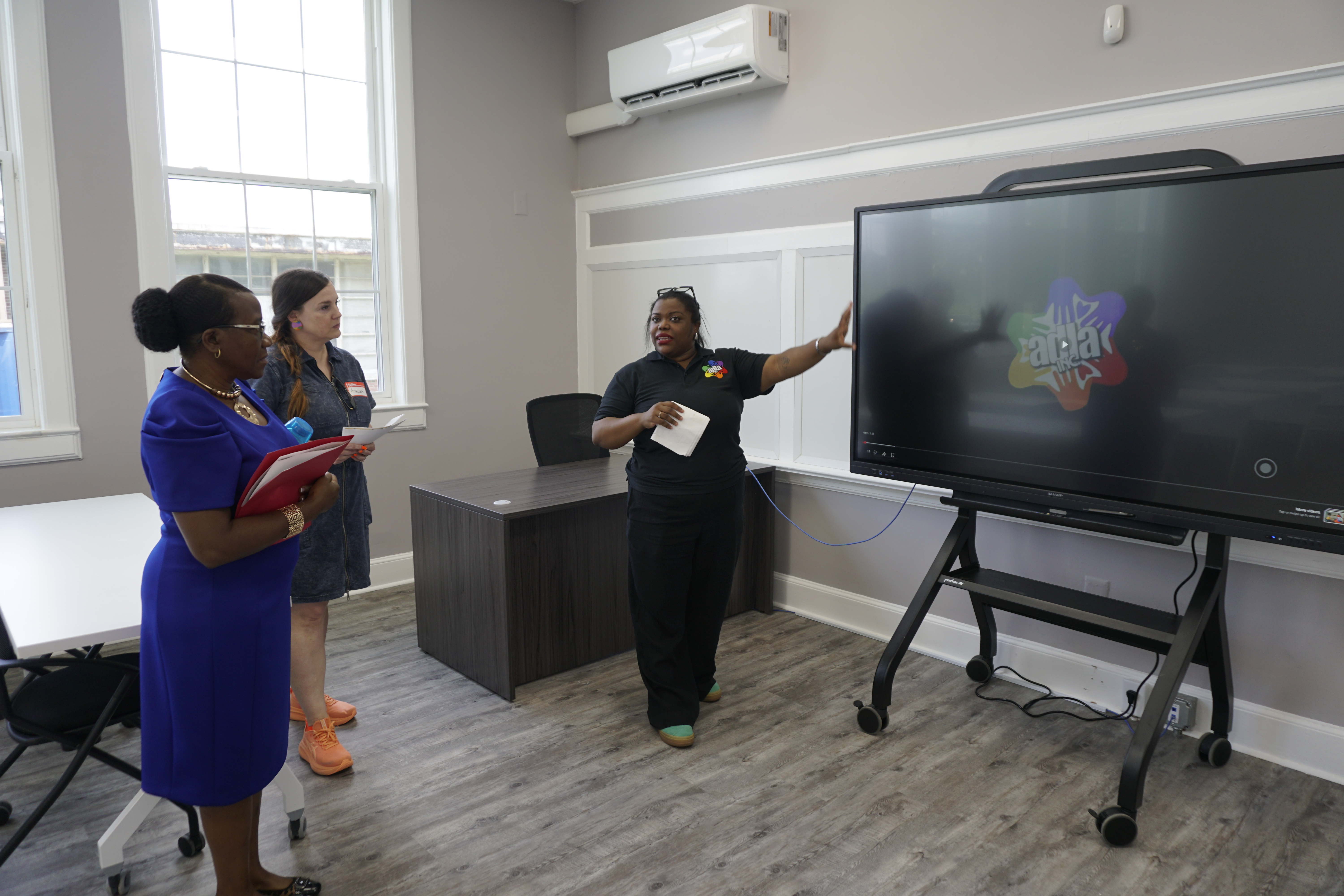Two women listening to another one in a conference in front of a screen