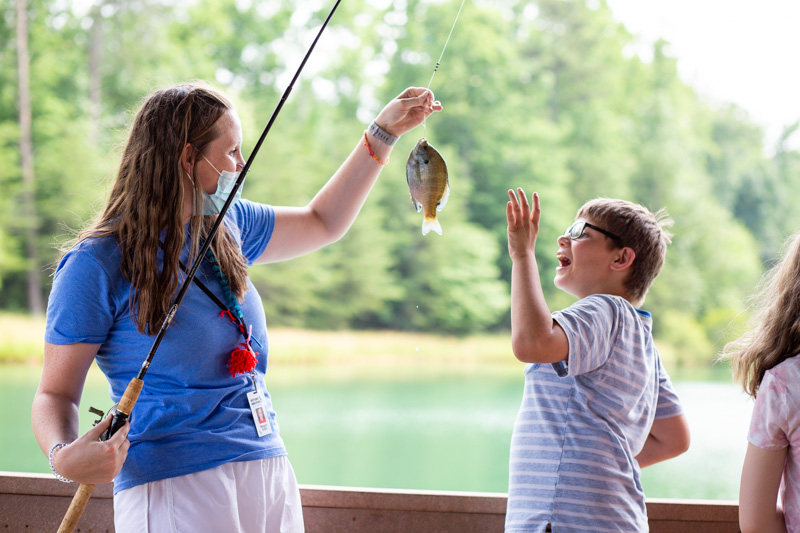 A woman showing a freshly caught fish to a kid