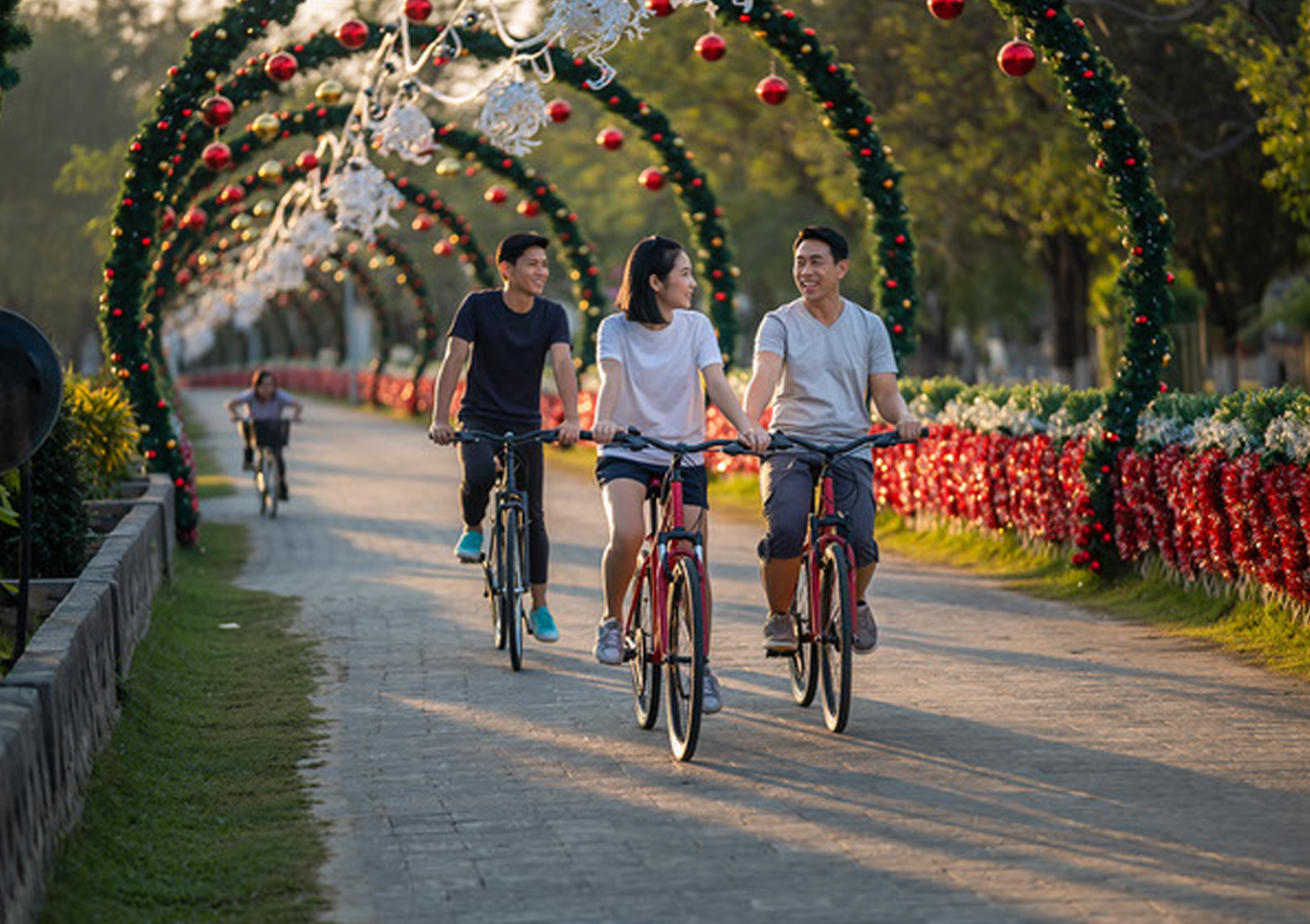 A photo of young people bicycling in a park with holiday decorations.