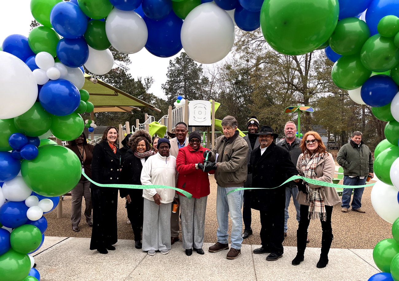 A pictures of the playground cutting ribbon with green, blue and white arc ballons on the background
