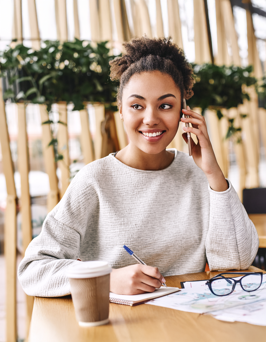 A woman sitting on a chair with a notebook and pen talking on the phone