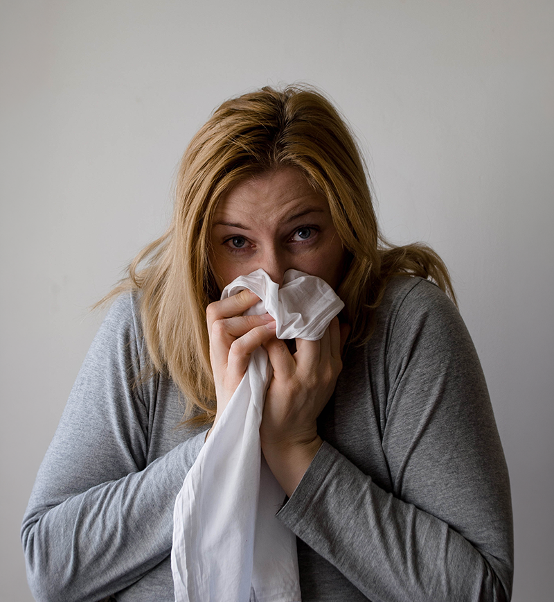 A woman with a napkin covering her nose and sneezing
